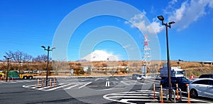 Ublic parking car with black light pole, high voltage electrical tower, wire, tree, blue sky and Fuji mountain background.