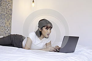 Shock asian beautiful girl work the laptop in the bed. Work from home concept