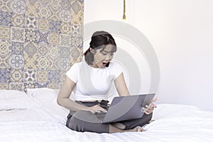 Shock asian beautiful girl work the laptop in the bed. Work from home concept