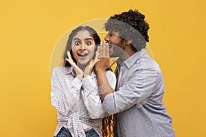 Shock, gossip, share advice. Young indian man whispering to lady on ear, surprised woman with open mouth
