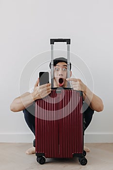Shock and surprise face of man using mobile phone application for travel, sitting with his baggage or luggage.