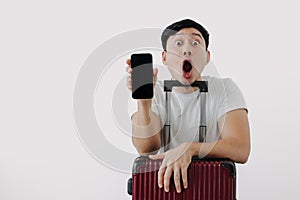 Shock and surprise face of man using mobile phone application for travel, sitting with his baggage or luggage.