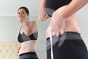 Shocked adult woman measuring waist circumference