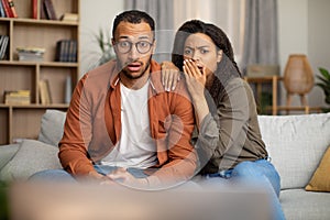 Shocked African American Couple Watching Shocking TV Content At Home
