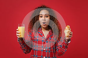 Shocked african american girl in pajamas homewear resting at home isolated on red background. Relax good mood lifestyle