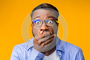 Shocked African American Guy Covering Mouth With Hand, Yellow Background