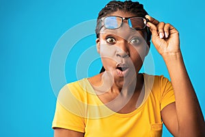Shocked African Woman Looking At Camera Rising Eyeglasses, Blue Background