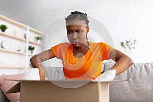 Shocked Afro woman unboxing delivery, upset because of shipping mistake, dissatisfied with online shopping service