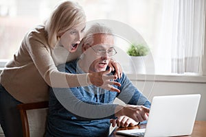 Shocked aged couple surprised by news at laptop online