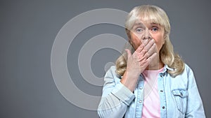 Shocked aging woman covering mouth with hand, astonished with news, emotions