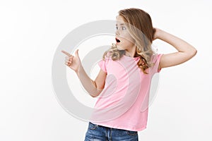 Shocked amazed cute blond little girl kid, touch head stunned, turn pointing left copyspace amazed, drop jaw wondered