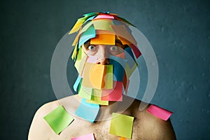 Shocked amazed man with colorful sticky notes all over his face over gray background