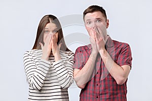 Shocked amazed young couple covering mouth with hands looking at camera