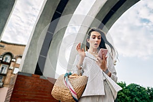 Shocked amazing woman woman looking on mobile phone in summer city street background