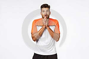 Shocked, anxious young handsome male athlete in sports t-shirt, gasping, cover mouth with arms and stare camera