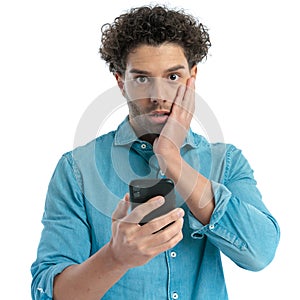 shocked arab man with curly hair holding phone and reading emails