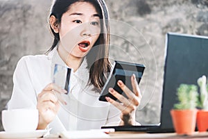 Shocked Asian woman hand counting expenses on calculator having problem with credit card