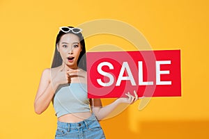 Shocked Asian woman pointing to red sale sign in hand