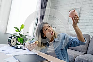 Shocked Asian woman seeing money less than expected in living room at home. Money saving concept