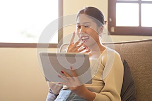 A shocked Asian woman is watching a movie on her digital tablet while relaxing on a couch