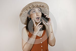 Shocked Asian woman wearing a straw hat talking on a mobile phone and laughing, expressing excitement emotions having a pleasant