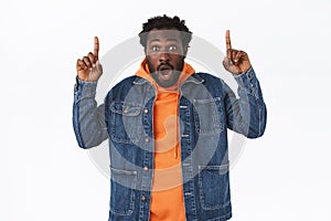 Shocked, astonished african-american bearded male customer in denim jacket, drop jaw gasping ambushed, pointing fingers