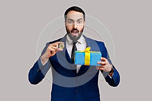 Shocked bearded businessman standing holding present box and golden bitcoin, crypto currency as gift