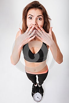 Shocked astonished young fitness woman standing on weighting scale