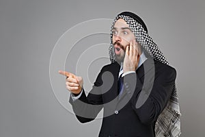 Shocked bearded arabian muslim businessman in keffiyeh kafiya ring igal agal classic black suit shirt isolated on gray