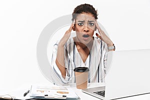 Shocked beautiful african woman posing isolated over white wall background using laptop computer drinking coffee