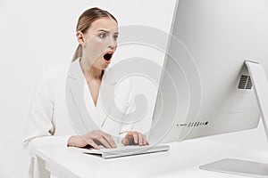 Shocked beautiful amazing woman sitting isolated over white wall background using pc computer