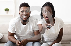 Shocked black couple watching tv with opened mouth