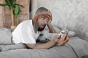 Shocked black man looking at clock in bed