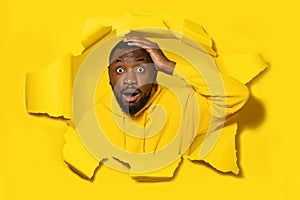 Shocked black man touching his head and looking through hole in yellow paper, free space