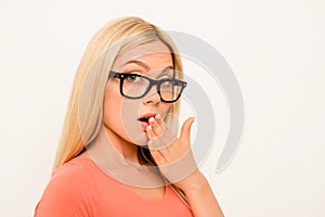 Shocked brainy girl in glasses holding hand near mouth