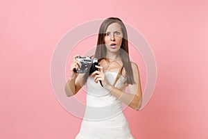 Shocked bride woman in white wedding dress holding retro vintage photo camera, choosing staff, photographer on