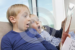 Shocked brother and sister reading storybook at home