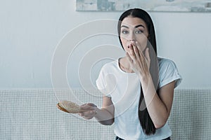 shocked brunette woman holding hairbrush and looking at camera hair