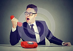 Shocked business man receiving bad news on the phone sitting at desk in his office