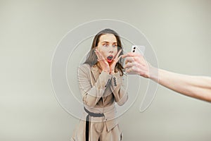 Shocked business woman looking at a smartphone screen with a surprised face, someone else`s hand holding a phone. isolated on