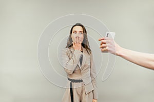 Shocked business woman in a suit looks at the smartphone screen in someone else`s hand and holds her face in surprise,  o