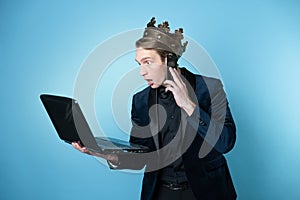 shocked businessman with a crown on his head uses a laptop and a phone.