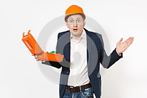 Shocked businessman in dark suit, protective hardhat holding opened case with instruments or toolbox and spreading hands