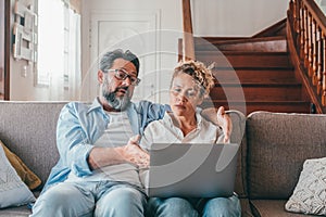 Shocked caucasian couple looking at laptop screen frustrated by unexpected bad news online. Husband and wife disappointed and