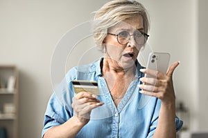 Shocked concerned mature woman in glasses holding credit card