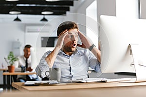 Shocked confused male manager using compuer and holding head