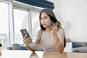 Shocked confused young Asian bank customer woman looking at smartphone
