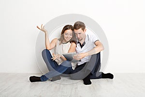 Shocked couple using laptop, sitting on floor