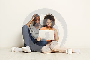 Shocked couple using laptop, sitting on floor