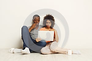 Shocked couple using laptop, sitting on floor